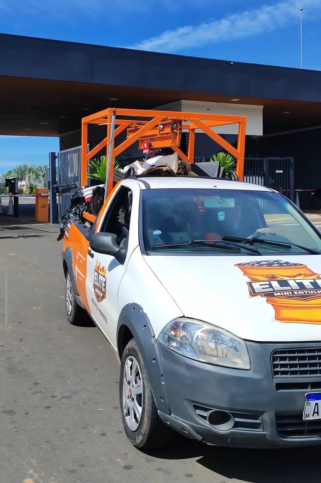 Veículo branco e laranja da Elite Mini Entulho em frente a um condomínio